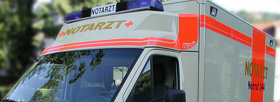 Weißer Notarztwagen mit rotem Kreuz und Blaulicht auf dem Dach.